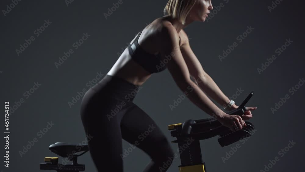 Young woman is engaged in a modern spin bike, performs aerobic endurance training on the simulator in the gym. Young woman is engaged in a modern spin bike, performs aerobic endurance training on the simulator in the gym.