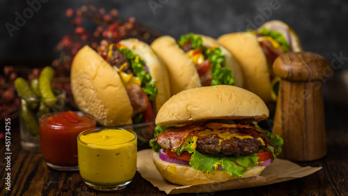 Selective focus on hamburgers with beef burgers and ketchup, pepper, mustard sauce, tomato sauce and cheese served fresh onions on a wooden board in loft background.
