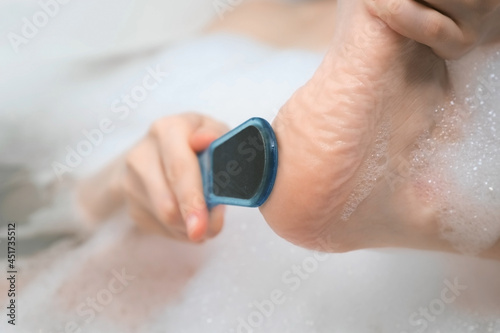 Woman is peeling her foot and toes using peeler sitting in bathroom at home, closeup view. Spa beauty treatment. Wellness, skincare and self love concept. Relaxing and enjoying time. Beauty procedure.