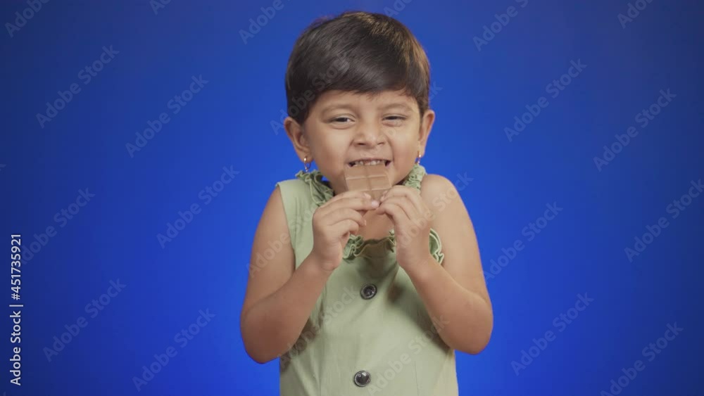 Happy girl kid enjoying chocolate bite by closing eyes on blue background - concepts of children's love and addictions on chocolates. Happy girl kid enjoying chocolate bite by closing eyes on blue background - concepts of children's love and addictions on chocolates.