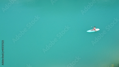 A girl in a dress floats on a glanders board on a pond with bright turquoise water. Warm summer day for travel. Top view from a quadcopter. Aerial photography