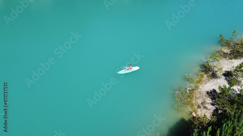A girl in a dress floats on a glanders board on a pond with bright turquoise water. Warm summer day for travel. Top view from a quadcopter. Aerial photography © Sergei Malkov
