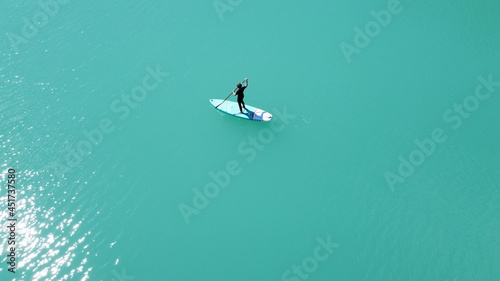 A girl in a dress floats on a glanders board on a pond with bright turquoise water. Warm summer day for travel. Top view from a quadcopter. Aerial photography