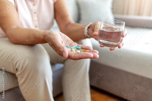 Senior woman takes medicines with glass of water. Old woman with pills and glass of water at home, closeup. Daily norm of vitamins, effective drugs, modern pharmacy for body and mental health concept.