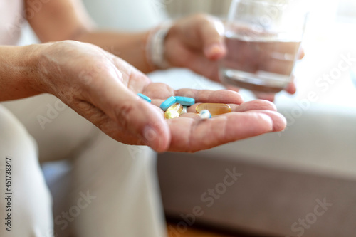 Close-up image of unrecognizable senior woman holding pills and glass of water  medicine and recovery treatment  copy space. Photo of a elderly woman taking daily medicine. Healthcare concept.