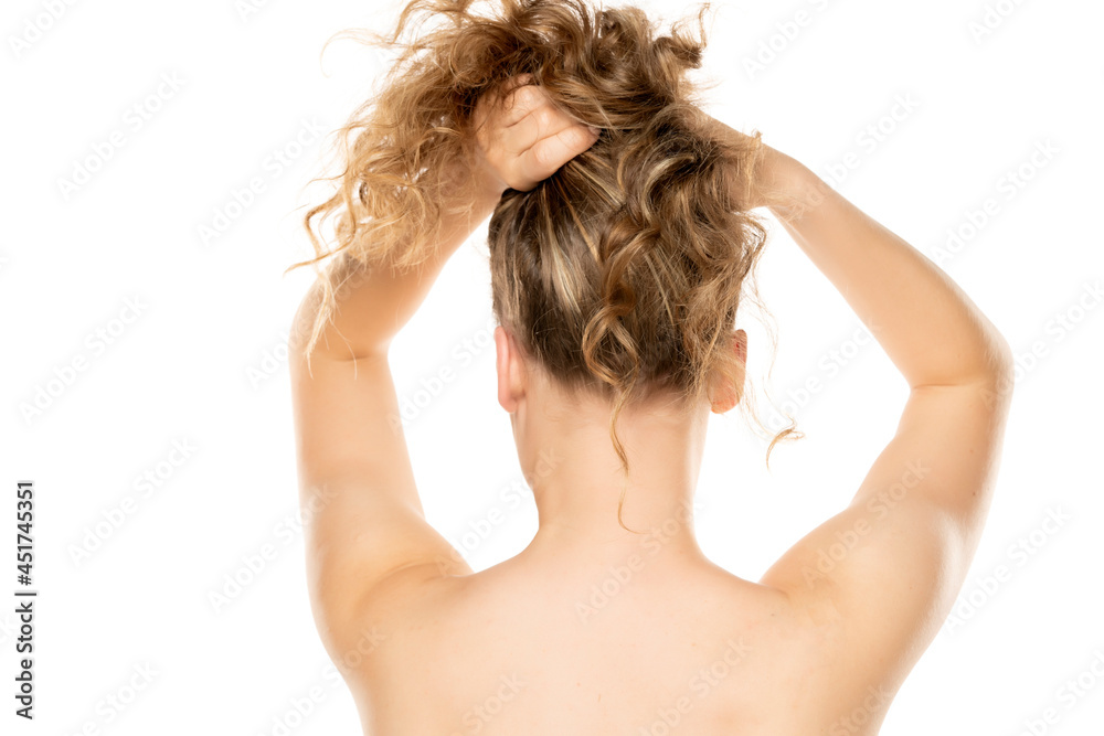 Rear view of a young blonde tying her hair to a white background Rear view of a young blonde tying her hair to a white background