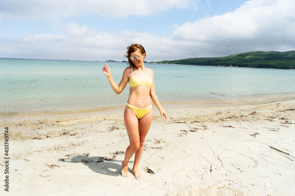 Portrait of happy tanned woman in sunglasses and yellow bikini smiling posing at sea beach Portrait of happy tanned woman in sunglasses and yellow bikini smiling posing at sea beach