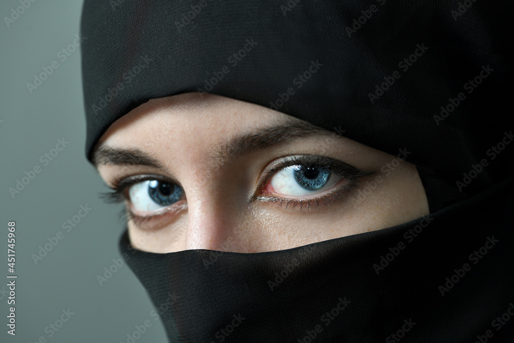 Naklejka premium The face of a young woman with large beautiful eyes, covered with a black Muslim veil. Close-up, selective focus.