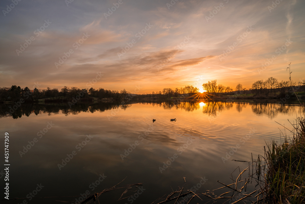Landschaft und Sonnenuntergang am Ufer im Westpark Donaupark in Regensburg mit Spiegelung des Himmels in dem glatten See mit wunderschönen dramatisch Farben Farbenspiel mit Wolken, Deutschland