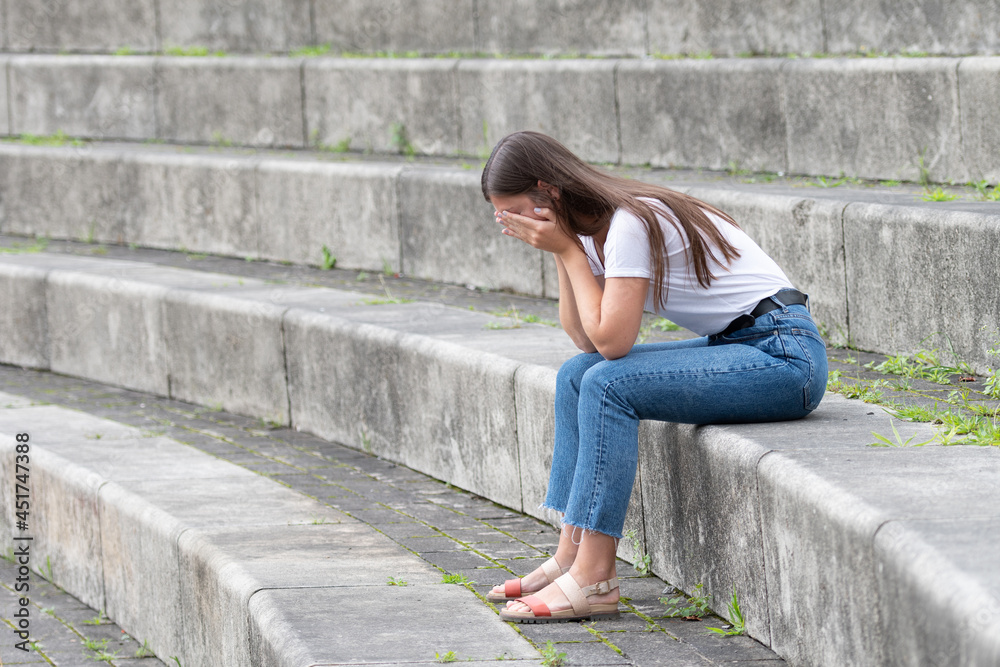 Young woman sitting on stairs covering her face and crying. Mourning, psychology and mental health concept Young woman sitting on stairs covering her face and crying. Mourning, psychology and mental health concept