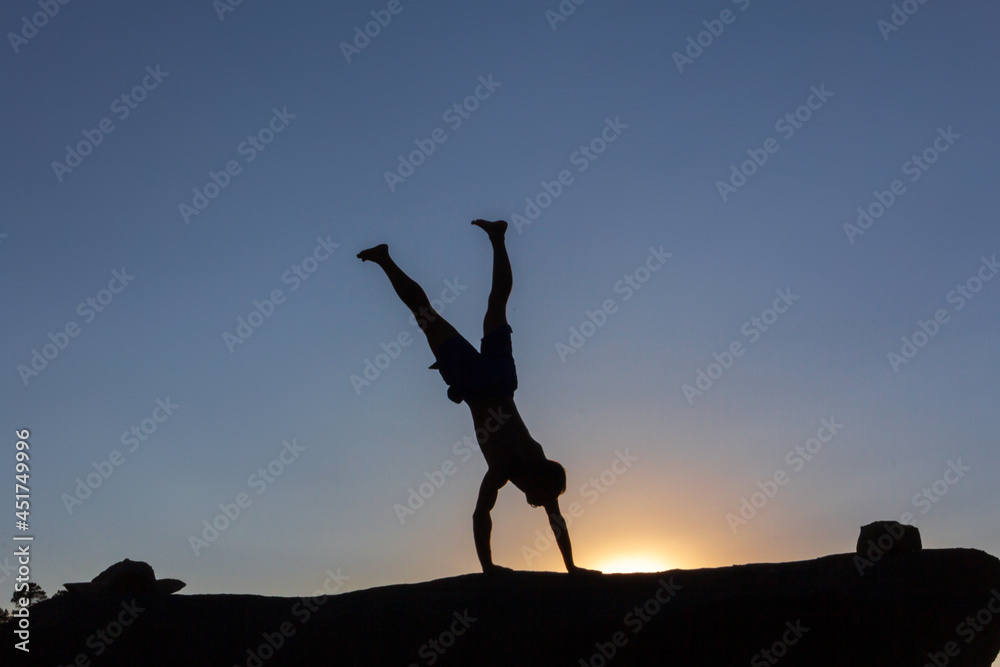 Boy doing acrobatics on a rock at sunset in autumn. Copy space. Backlight.