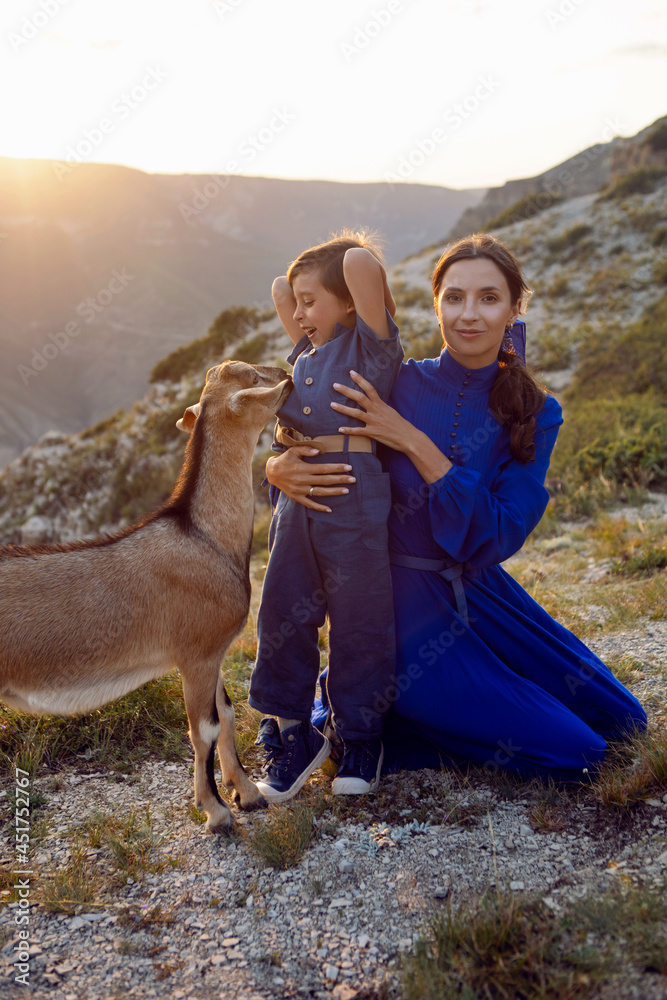 boy and his mother in a dress walk through the mountains with a goat at sunset in Dagestan