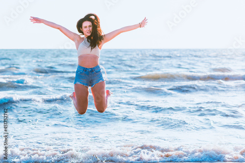 Jumping happy girl on a beach, fit sporty sexy body, woman enjoys sunset freedom, vacation, summertime fun concept.Toned