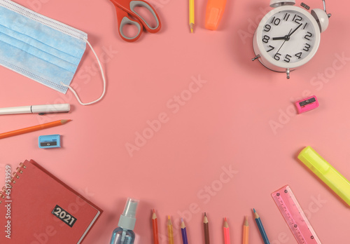 flat lay of school accessories with 2021 red book, medical face mask and alcohol spray bottle on pink background. Covid19 protection and back to school concept.