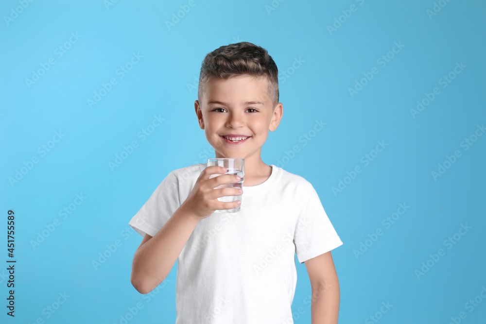Cute little boy with glass of water on light blue background Cute little boy with glass of water on light blue background