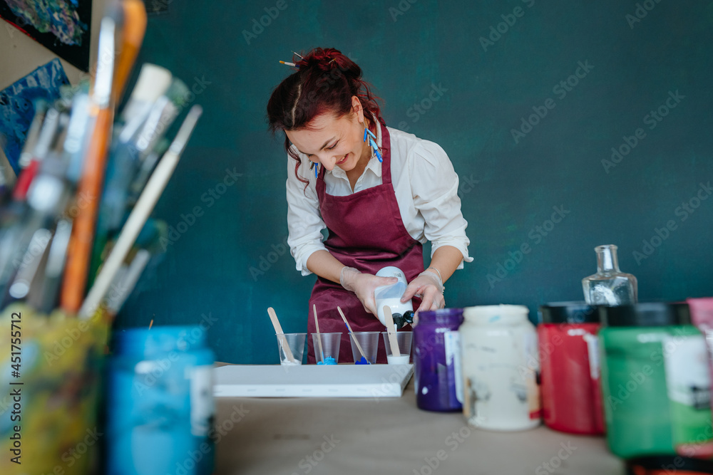 Female artist pouring acrylic medium for painting picture in fluid pouring  technique Stock Photo