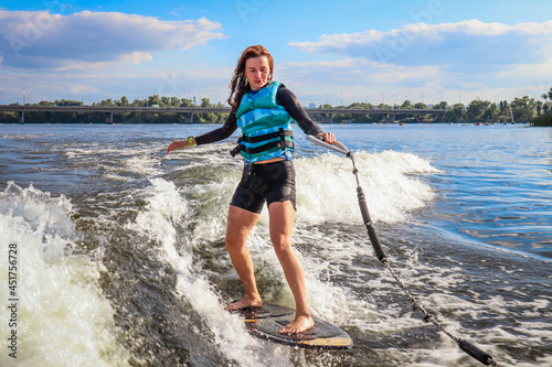 The girl is learning to ride a wakesurf on the river behind the boat. Wake vest. Board photo
