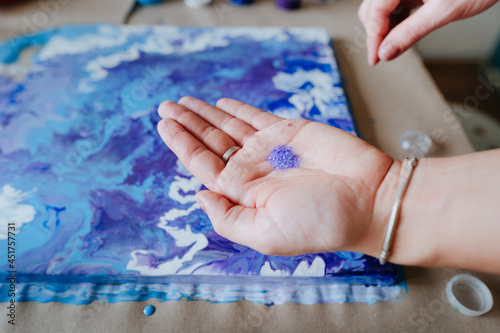 Female artist's hand sprinkling silver glitter on the fluid art picture