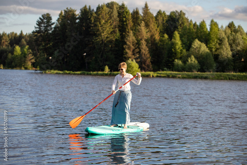 A young girl in a skirt rides a SUP board on a forest pond © Sergei Malkov