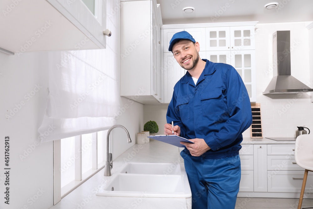 Professional plumber with clipboard checking water tap in kitchen