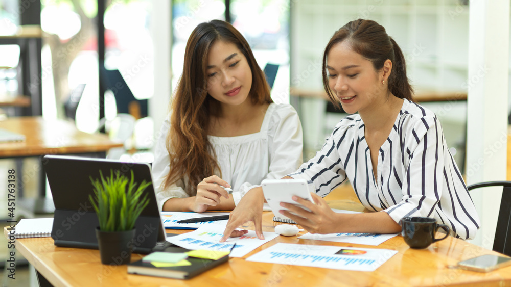 two casual asian businesswomen discussing work in office two casual asian businesswomen discussing work in office