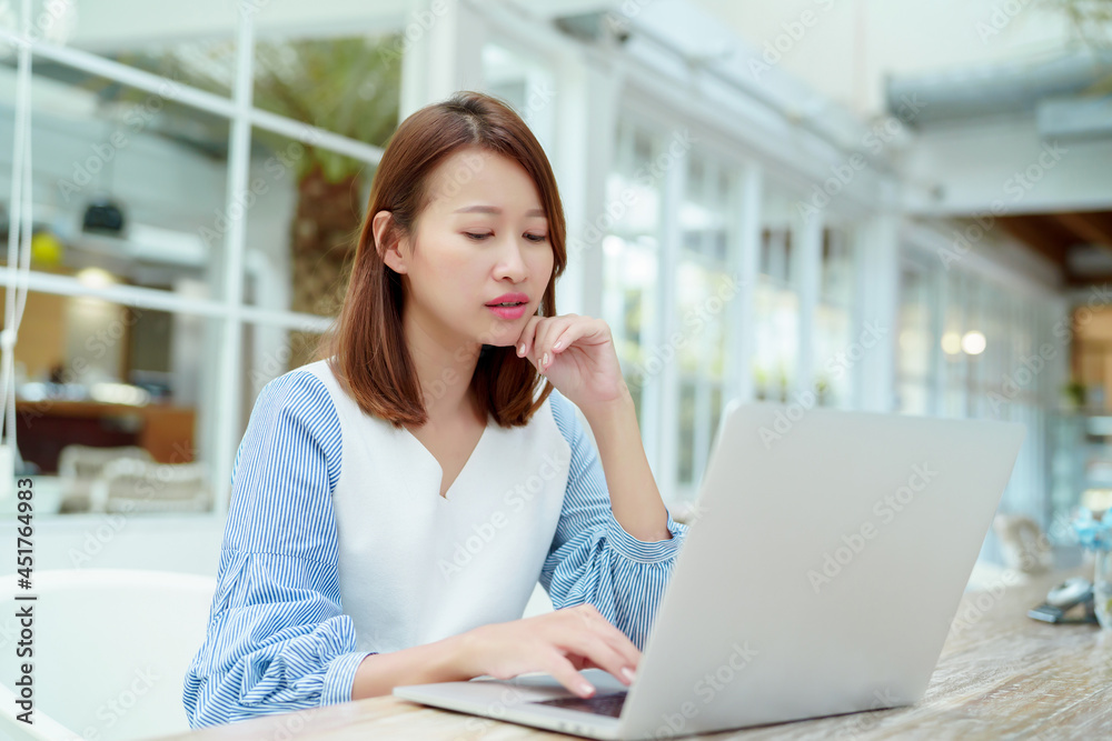 A beautiful woman wearing an Asian white shirt is sitting in front of a laptop computer shopping online with a happy smile in a bakery shop. A beautiful woman wearing an Asian white shirt is sitting in front of a laptop computer shopping online with a happy smile in a bakery shop.