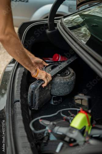 Handsome man getting ready for a vacations, loading his backpack in a car trunk, together with a drone and other camera equipment.