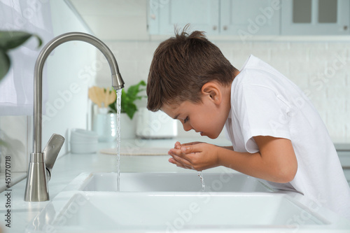 Obraz na płótnie Boy drinking tap water over sink in kitchen