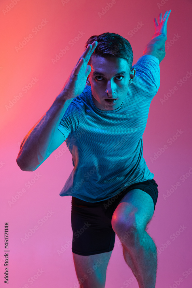 Close up Caucasian professional male athlete, runner training isolated on pink studio background with blue neon filter, light. Muscular, sportive man. Close up Caucasian professional male athlete, runner training isolated on pink studio background with blue neon filter, light. Muscular, sportive man.