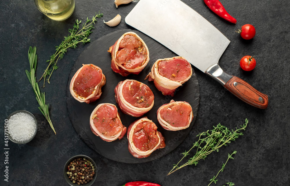 raw pork tenderloin medallions wrapped in bacon on a stone background