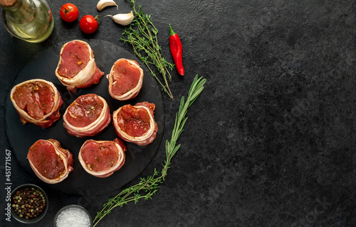 raw pork tenderloin medallions wrapped in bacon on a stone background with copy space for your text 