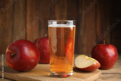Glass of delicious cider and ripe red apples on wooden table