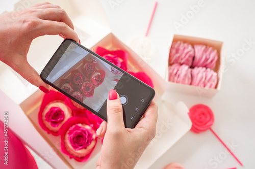 Woman is taking photo of homemade sweets, cupcakes and marshmallows using her smartphone. Food blogger is making content. 