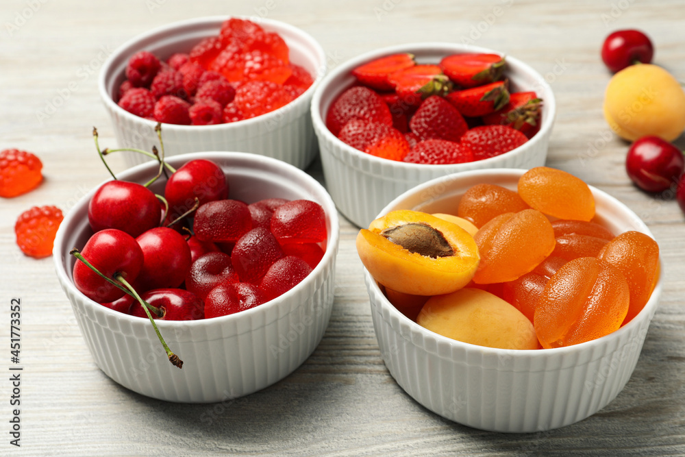 Delicious gummy candies and fresh fruits on white wooden table Delicious gummy candies and fresh fruits on white wooden table