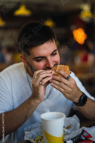 Chico joven guapo comiendo hamburguesa en restaurante americano