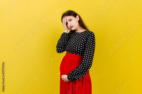 Beautiful young pregnant woman feeling head ache on colored background isolated. Stressed pregnant woman or mother problems