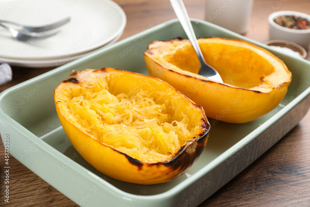 Halves of cooked spaghetti squash in baking dish on wooden table, closeup Halves of cooked spaghetti squash in baking dish on wooden table, closeup