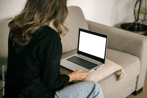White screen on laptop. Mock up. Young woman working remotely on laptop computer at cozy home on couch