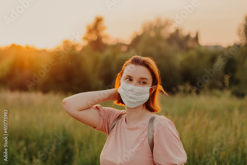 Redhead girl young woman wearing face mask walking alone in summer meadow and dreaming about theend of lockdown New reality routine.