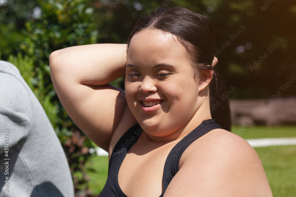Portrait of young biracial woman with Down Syndrome in active wear tying her hair and smiling Portrait of young biracial woman with Down Syndrome in active wear tying her hair and smiling