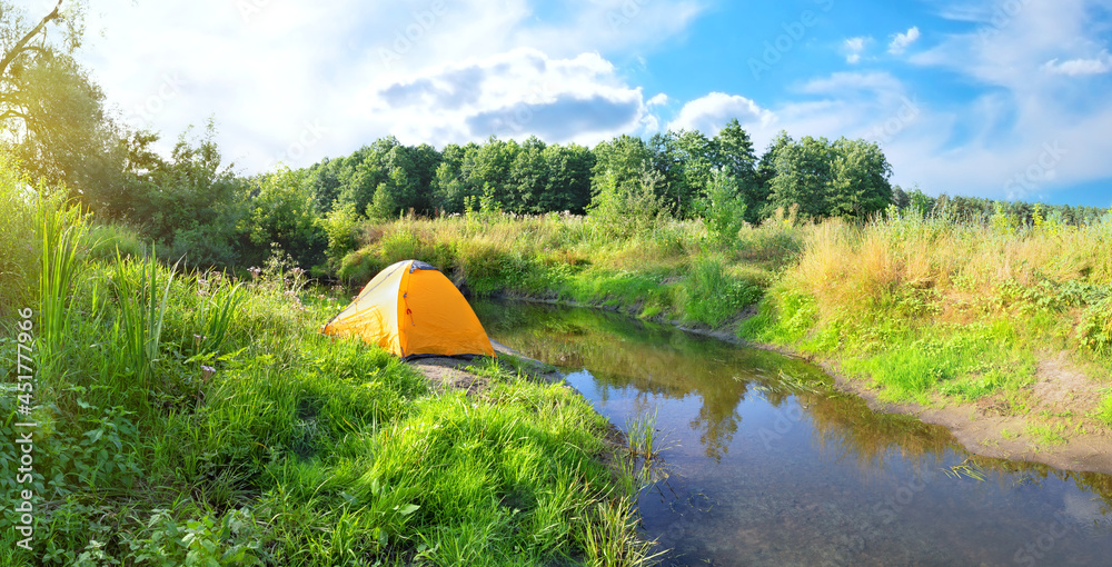 Orange tent on banks of small river with green banks
