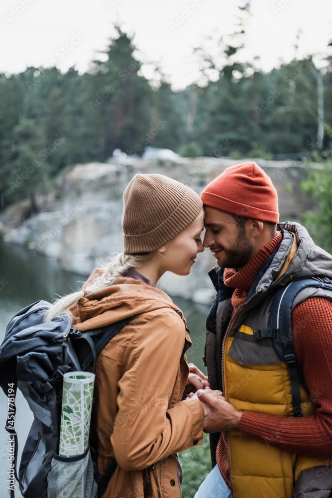 young and joyful couple with closed eyes holding hands near lake in forest