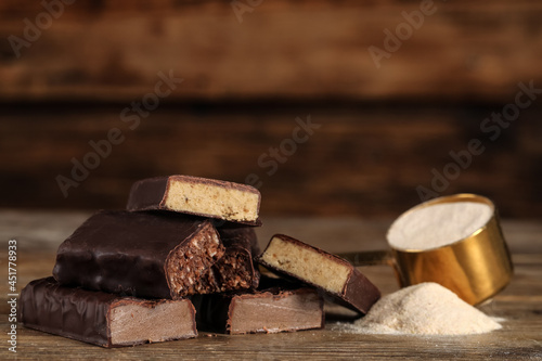 Pieces of tasty bars and scoop with protein powder on wooden table. Space for text