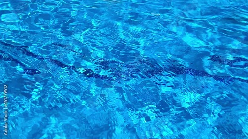 Water surface of a swimming pool. Water is moving making many reflections and ripples in an abstract  hypnotic manner.The bottom of is light blue and there is a darker blue line of tiles going across. photo