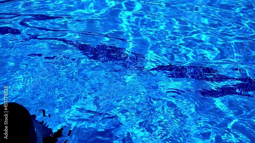 Shot of the surface of a swimming pool. A woman's legs are seen moving up and down as she relaxes feeling the water through her legs. The water is light blue and reflecting light.  photo