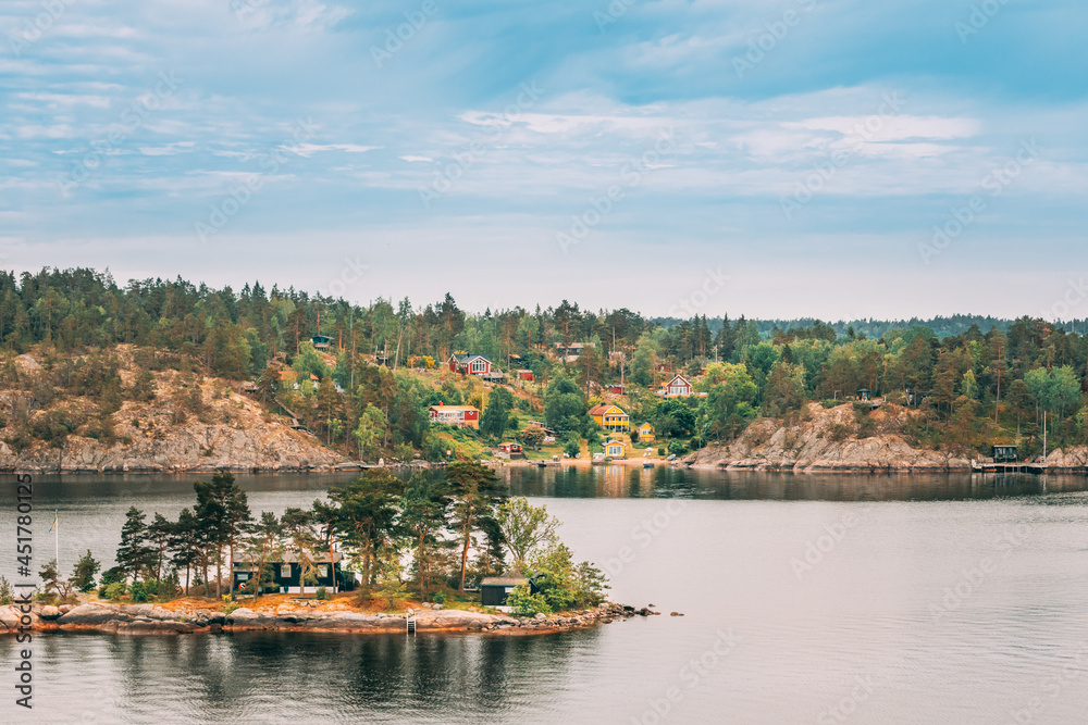 Sweden. Many Beautiful Swedish Wooden Log Cabins Houses On Rocky Island Coast In Summer Day. Lake Or River Landscape