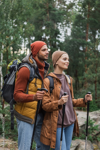 pleased young couple with backpacks trekking together with hiking sticks