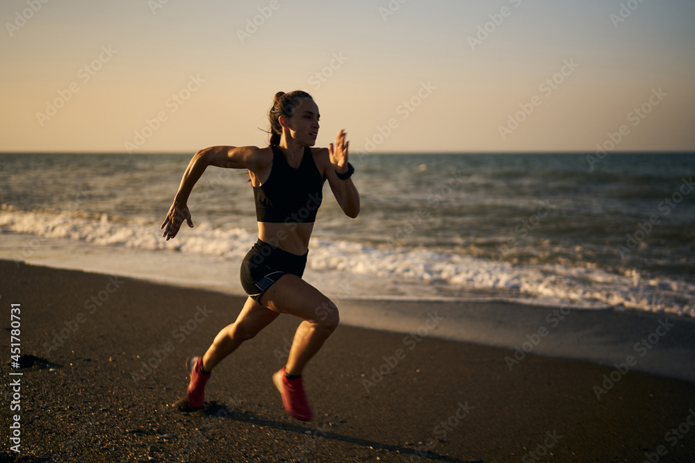 young professional female athlete running on a sunrise in the beach