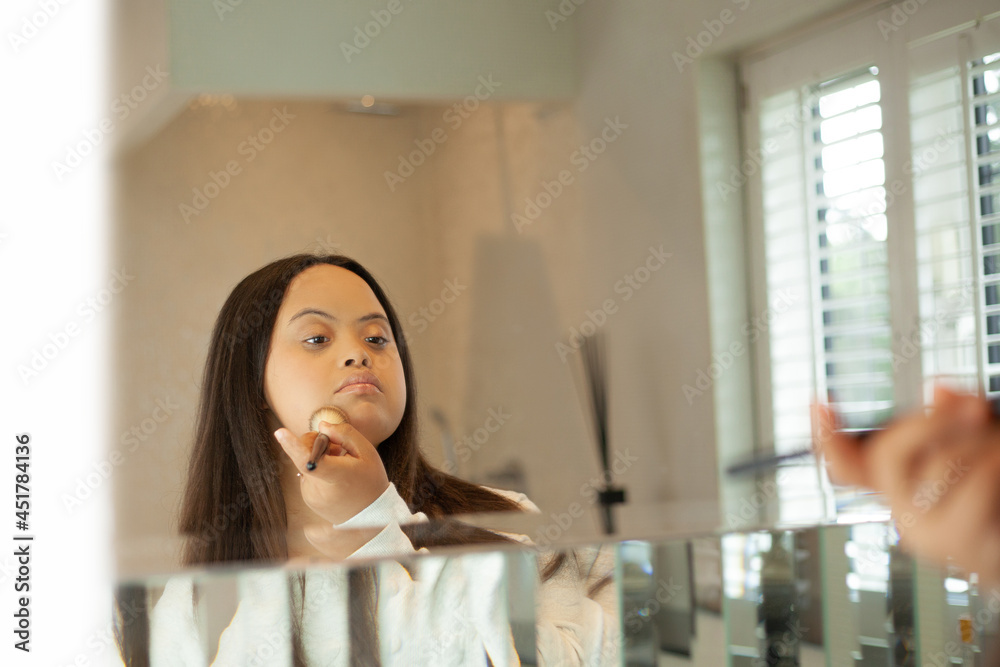 Young biracial woman with Down Syndrome applying make-up with brush in the bathroom