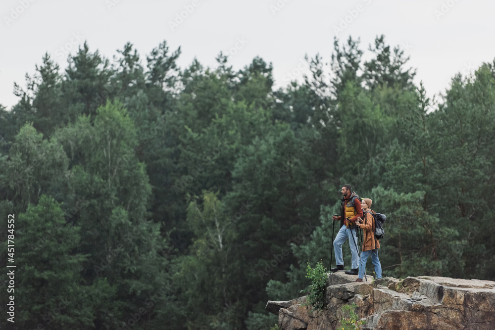 couple with hiking sticks standing on rocky cliff